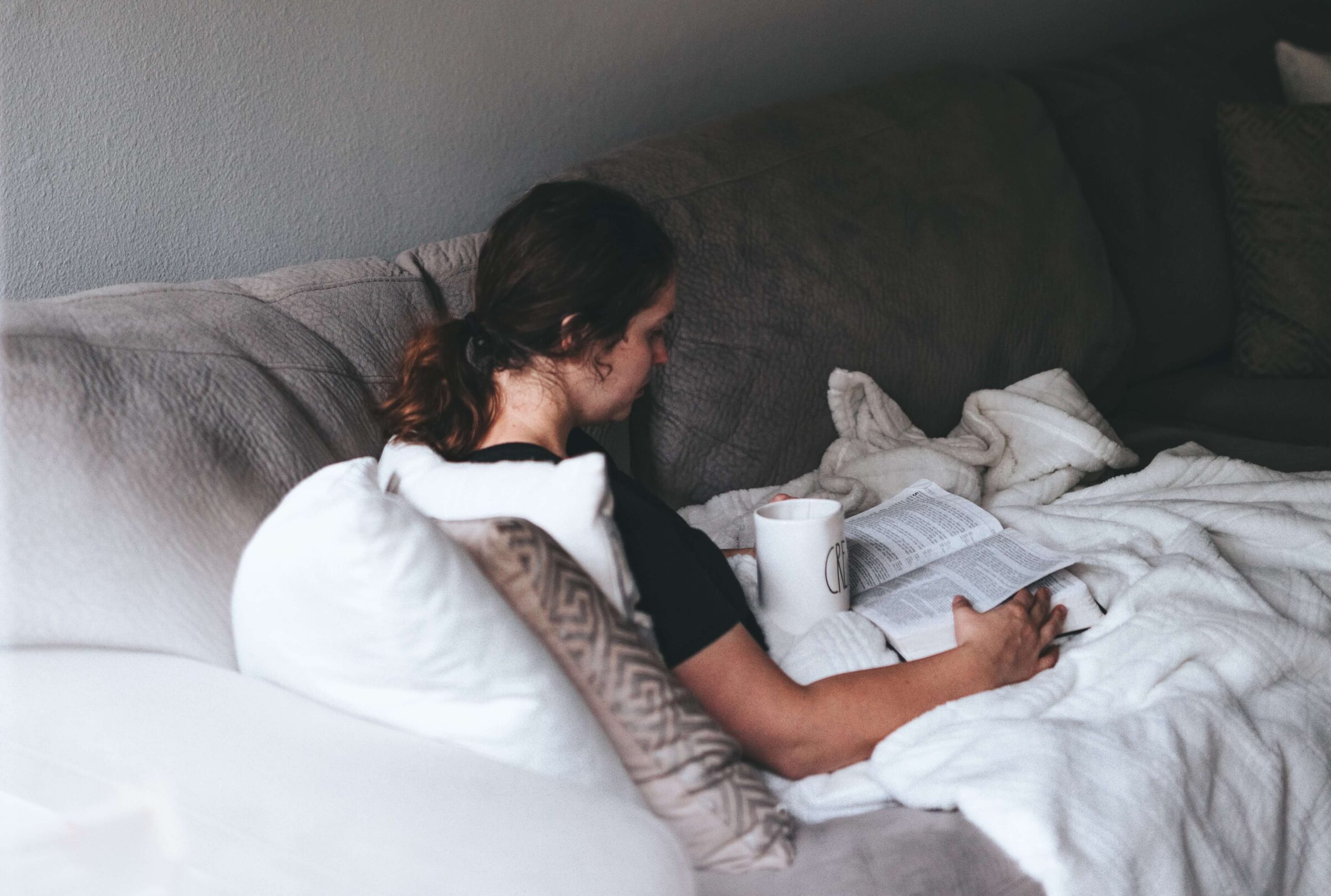 woman reads under blankets on couch