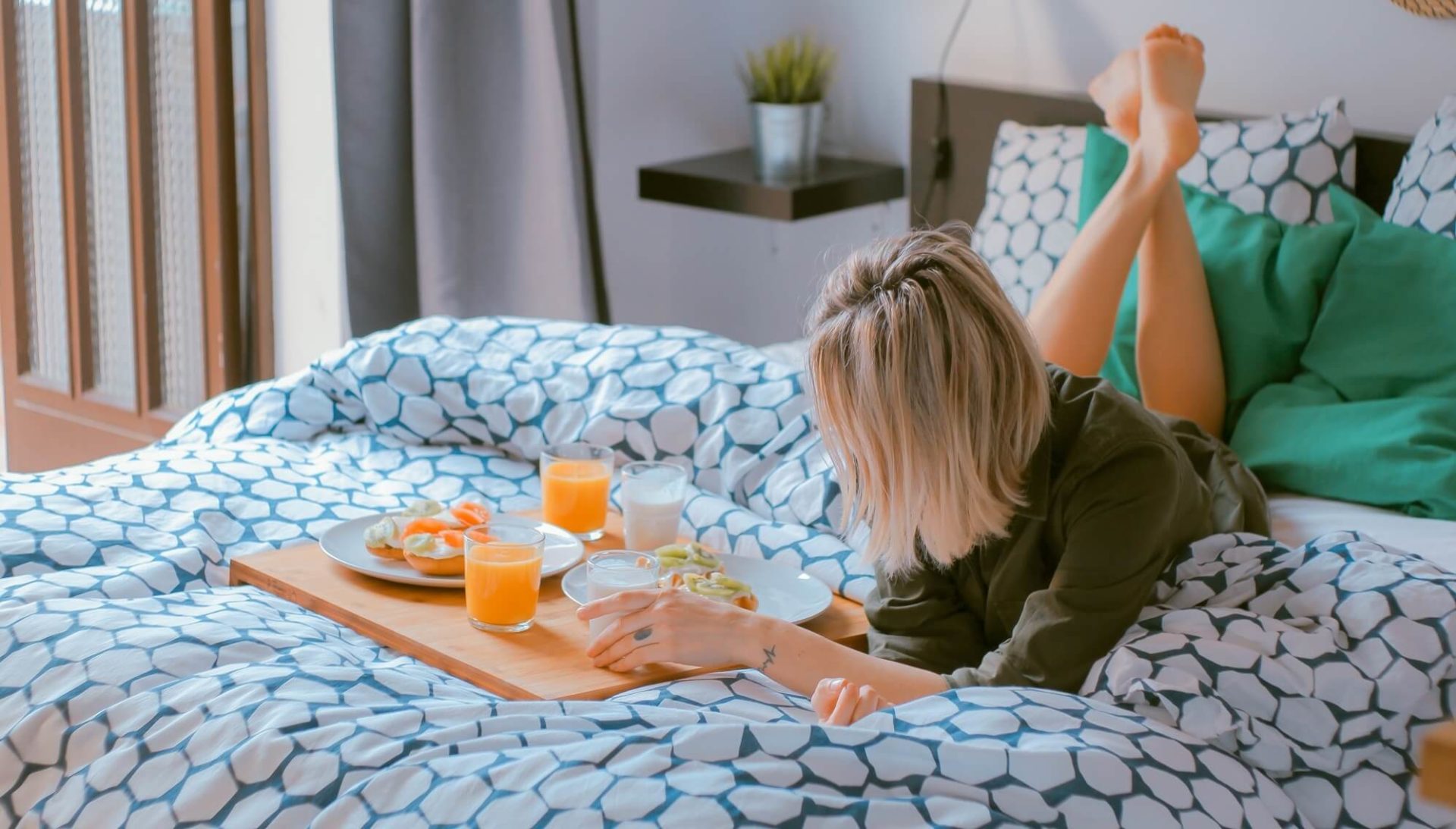 woman lays on bed with hand on tray of breakfast items
