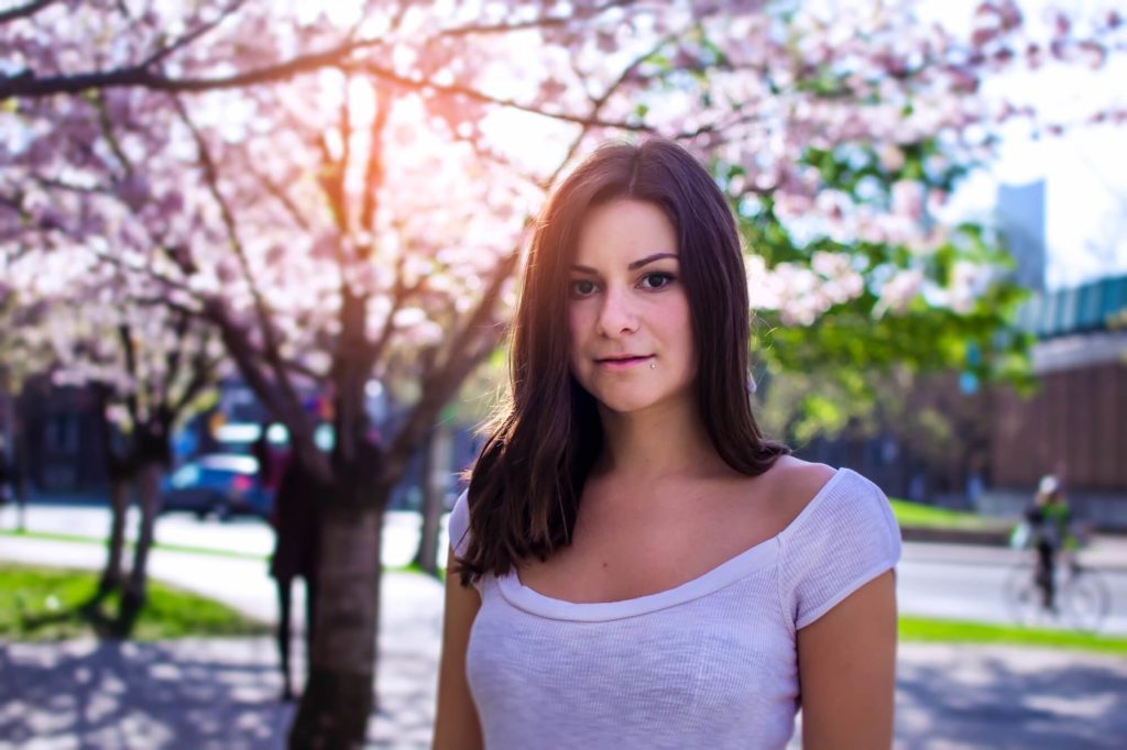 woman with brown hair in white t shirt stands in front of tree