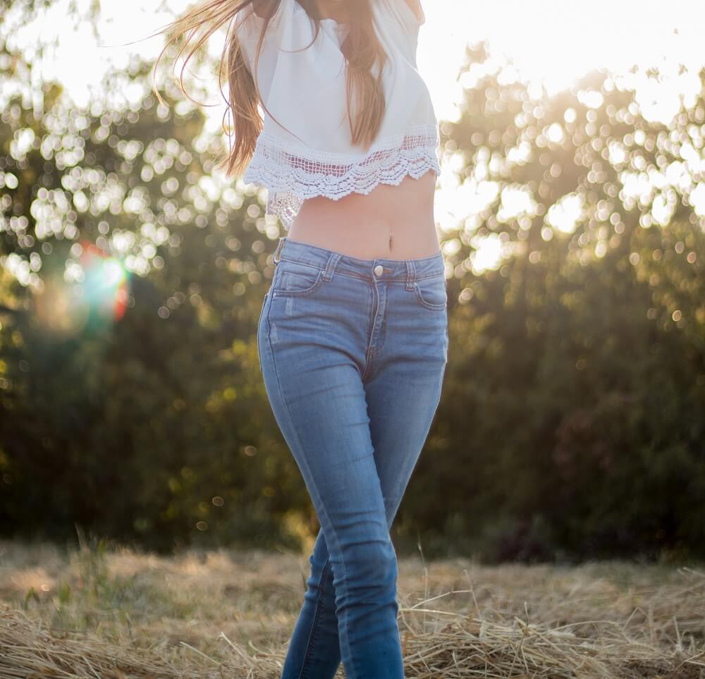 woman in blue jeans and white shirt with midriff showing